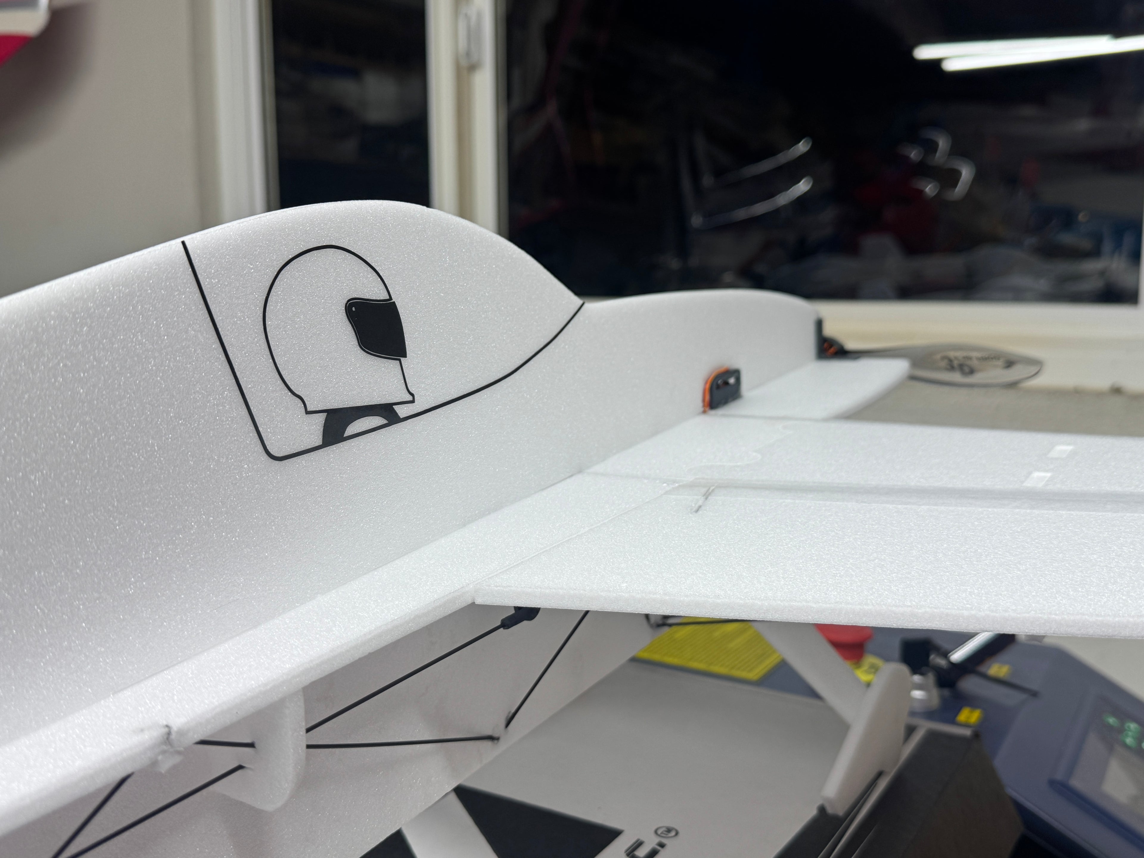 Close-up of a white model airplane with a logo on a blurred indoor background