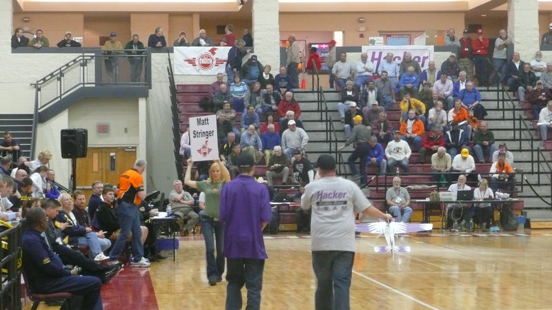 Indoor RC Plane competition in progress with pilots and spectators in a gymnasium.