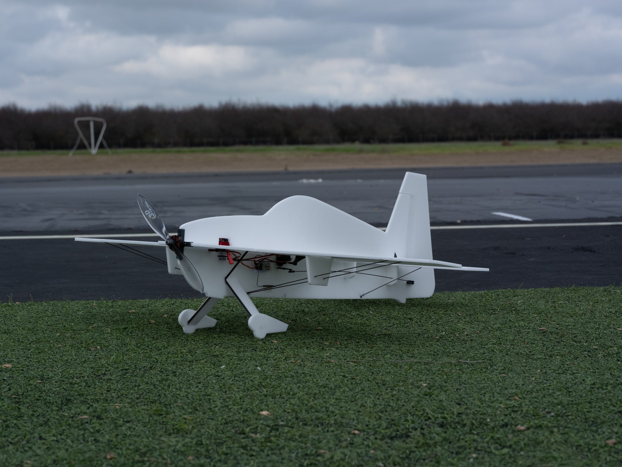 White foam model plane on a grassy area with a runway in the background