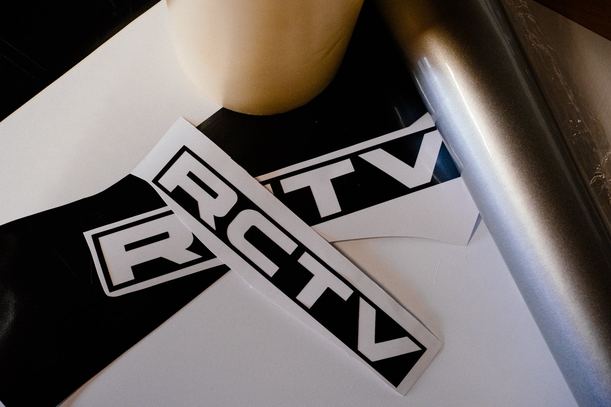 Two 'RCTV' stickers on a white surface with a pen and object in the background.