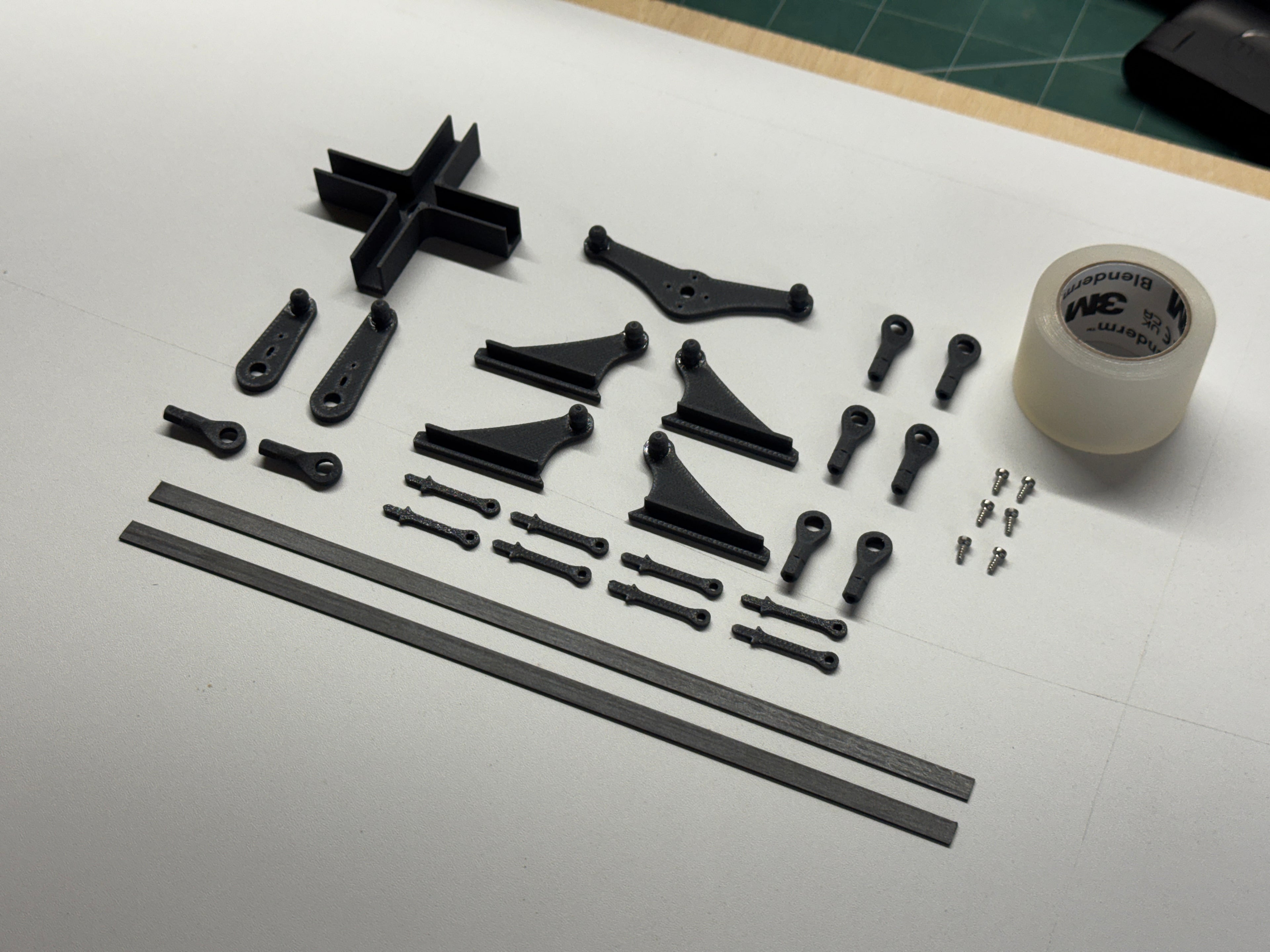Set of black mechanical parts on a white surface with tape in the background