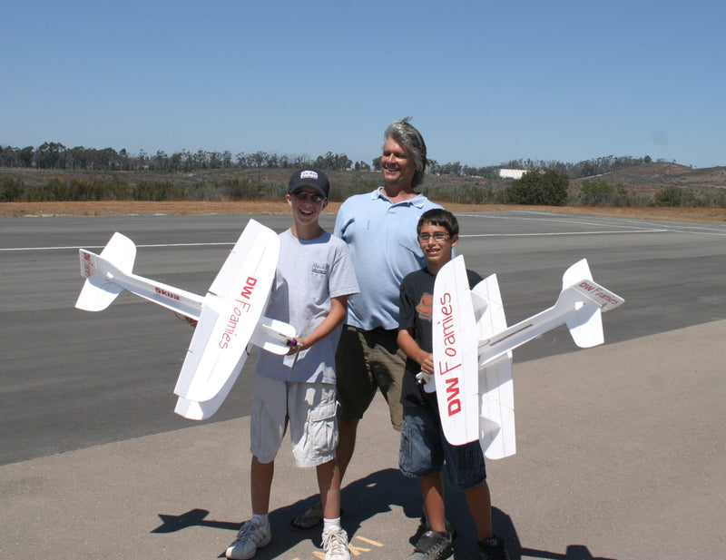 Three people holding model airplanes on an airstrip with a clear sky.