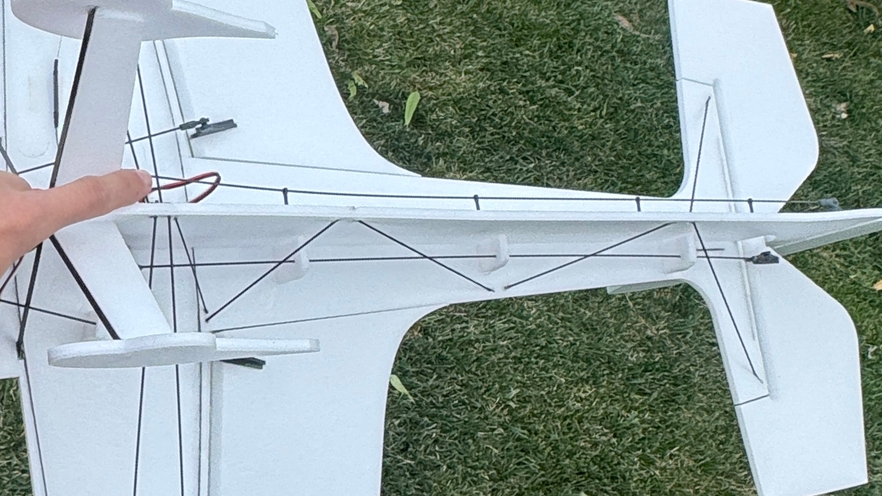 Close-up of a white model airplane on grass with a hand pointing at it