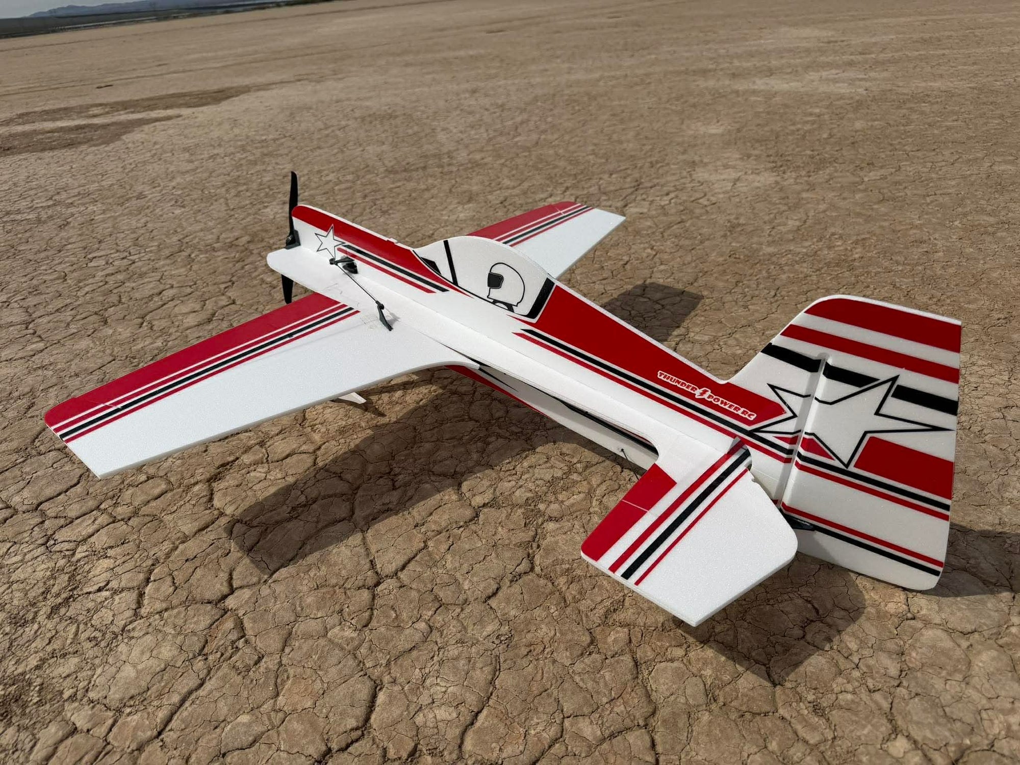Model airplane with red and white design on a dry, cracked earth surface