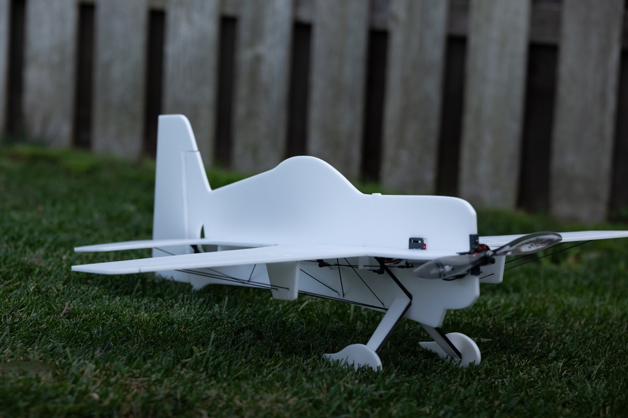 White foam model airplane on grass with a wooden fence in the background