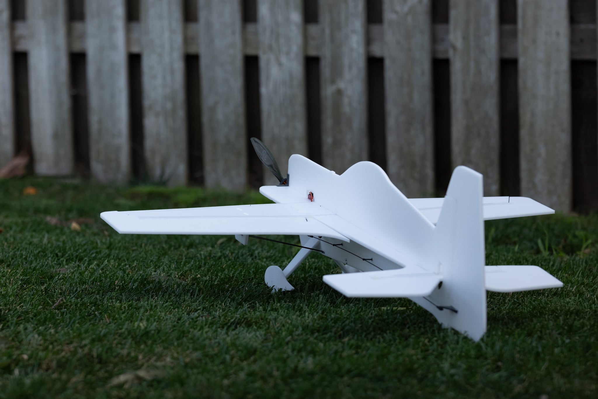 White foam model airplane on grass with a wooden fence in the background