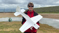 Matt Stringer holding a large white model airplane outdoors with a cloudy sky and landscape in the background.