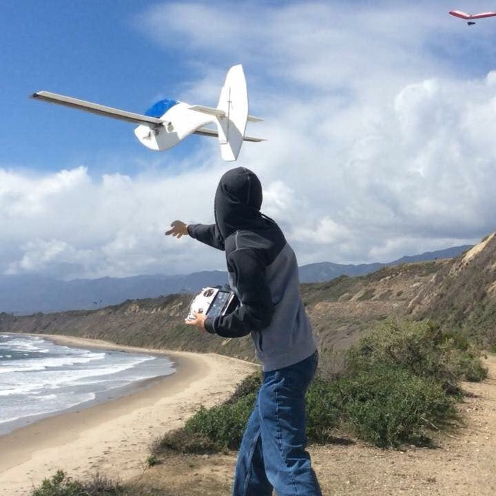 Person launching a remote-controlled airplane on a beach with mountains in the background